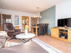 Una sala de estar moderna con un sofá, una mesa de comedor con sillas, un televisor y un mueble de madera con dispositivos electrónicos.