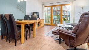 A modern living room with a dining area, a sofa, and a TV. - Spacious Möwennest vacation apartment with terrace, garden view and pool in Zingst (Zingst)