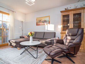 A modern living room with a sofa, a recliner, and a coffee table. There is a painting on the wall and a cabinet with glass doors. - Spacious Möwennest vacation apartment with terrace, garden view and pool in Zingst (Zingst)