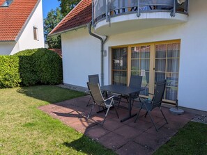 A patio with a table and chairs, a covered outdoor area, and a white building with a red roof.