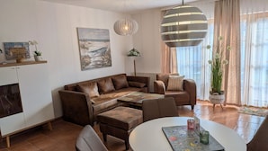 A living room with a brown leather sofa, a white coffee table, and a hanging light fixture. - Comfortable vacation apartment surrounded by greenery with terrace and pool in the Zingst vacation park - (Zingst)