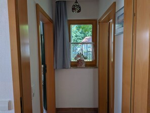 Un pasillo estrecho con puertas de madera, una ventana con cortina y una lámpara colgante.