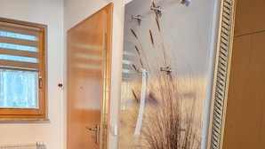 A room with a wooden door, a radiator, a window with blinds, and a wall with a textured design and a hanging plant. - Comfortable vacation apartment surrounded by greenery with terrace and pool in the Zingst vacation park - (Zingst)