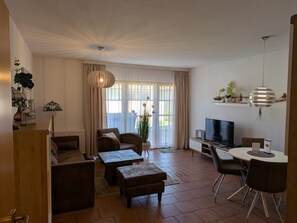 A living room with a sofa, coffee table, TV, and a dining area with chairs.