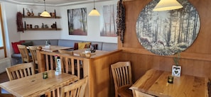 Een gezellig restaurantinterieur met houten tafels en stoelen, hanglampen en kunstwerken met bosmotieven aan de muren.