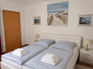 Een tweepersoonsbed met gestreepte lakens, twee nachtkastjes met lampen, en twee ingelijste foto’s aan de muur.