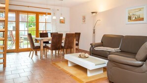 A modern living room with a brown leather sofa, a white coffee table, and a dining area with wooden chairs and a table.