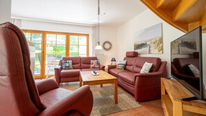 Een woonkamer met twee rode leren banken, een houten salontafel en een televisie op een houten dressoir.