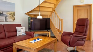 Een woonkamer met een houten trap, een televisie, een rode bank, een houten salontafel en een rode leren fauteuil.