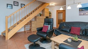 En moderne stue med en trappe i træ, lædermøbler og havudsigt gennem en glasdør.
