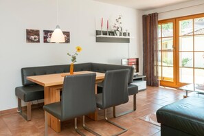 Un coin repas avec une table en bois, des bancs noirs rembourrés et un vase rempli de fleurs jaunes.
