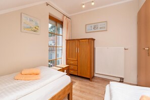 Ein Schlafzimmer mit einem Bett, einem Holzschrank, einem Fenster mit Vorhängen, einem Heizkörper und einer Wanduhr.