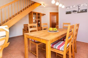 Ein Holztisch mit Stühlen, eine Obstschale und eine Treppe zu einem Raum mit einem Holzschrank und einer Tür.