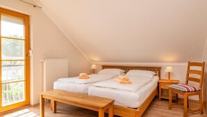A cozy bedroom with a wooden bed, two bedside tables, a bench, and a chair. - Comfortable terraced house with terrace, garden and pool in the Freesenbruch vacation park (Zingst)