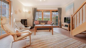 A spacious living room with a sofa, two lounge chairs, a coffee table, and a TV. - Comfortable terraced house with terrace, garden and pool in the Freesenbruch vacation park (Zingst)