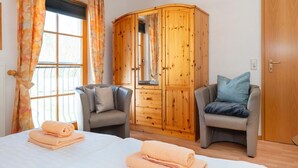 A hotel room with a bed, two armchairs, a wooden wardrobe, and a window with curtains. - Comfortable terraced house with terrace and garden in the Freesenbruch vacation park - (Zingst)