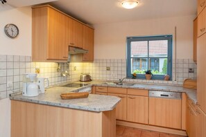 A kitchen with wooden cabinets, a built-in dishwasher, a window with a view, and a clock on the wall.