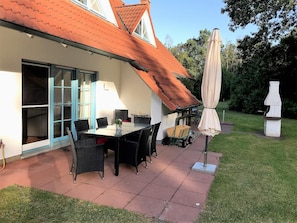 A patio with a table and chairs, a covered umbrella, and a small garden area with a statue.