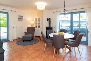 A dining area with a round table, grey chairs, a small ottoman, a cabinet with glass doors, a fireplace, and a view of parked cars through large windows.