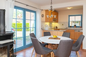 A kitchen with a round table, chairs, a stove, and a view through large windows.
