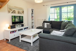A living room with a television, white entertainment unit, grey sofa, and a window with curtains.