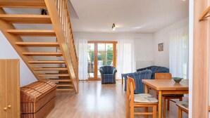 Un vaste espace de vie agrémenté d’un escalier en bois, d’une table à manger avec des chaises, d’un canapé et d’un panier en osier.