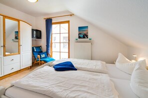 Een slaapkamer met twee bedden, een stoel, een televisie en een raam met gordijnen.