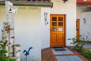 A building entrance with a wooden door, a welcome sign, and a bird mural. - Comfortable terraced house with terrace in the Freesenbruch vacation park near the sandy beach (Zingst)