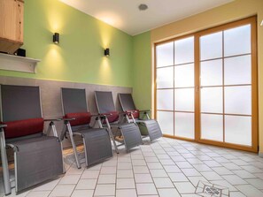 A room with a green wall, a large window with frosted glass, and several reclining chairs with red cushions.