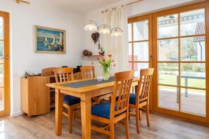 Een eetgedeelte met een houten tafel, blauw gestoffeerde stoelen, een vaas met bloemen en een schilderij aan de muur.