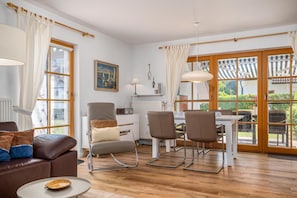 A modern living room with a sofa, chairs, a dining table, and a view of the garden through large windows.