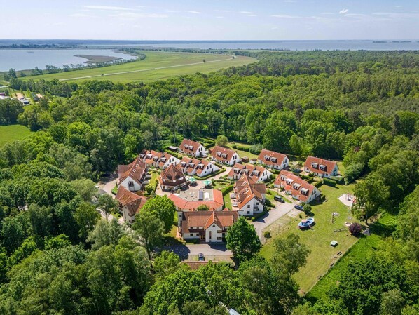An aerial view of a residential area with houses, surrounded by dense greenery and a body of water in the background.