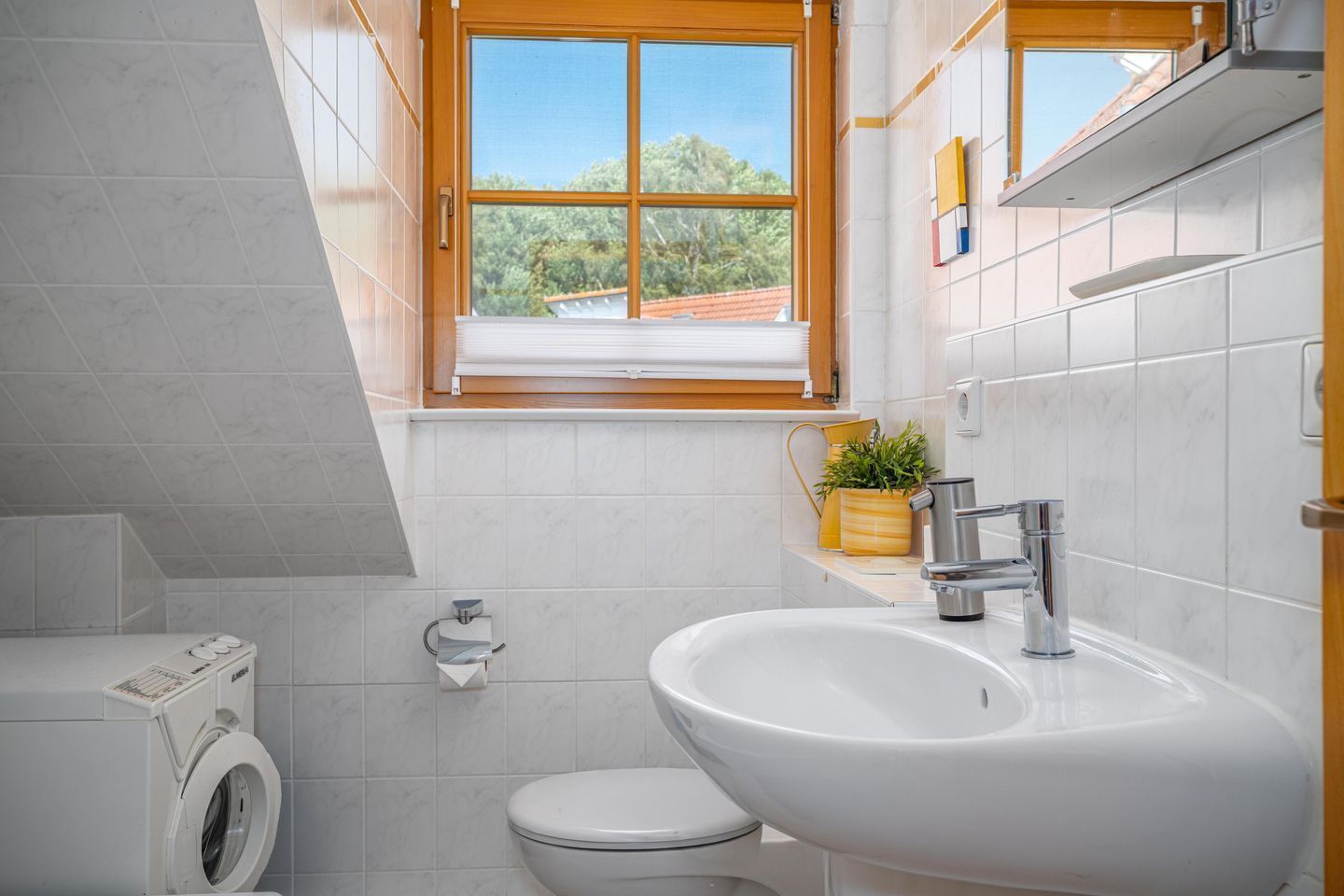 A modern bathroom with a washing machine, toilet, sink, and a window with a view.