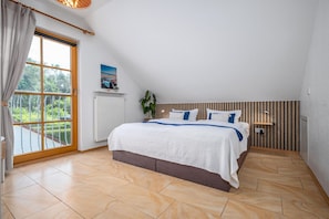 A bedroom with a large bed, a window with curtains, a radiator, a plant, and a wooden wall panel. - Cozy townhouse with a terrace in the Freesenbruch vacation park near the sandy beach (Zingst)