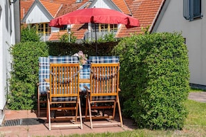 Two wooden chairs with plaid cushions, a red umbrella, and a hedge in a garden setting. - Cozy townhouse with a terrace in the Freesenbruch vacation park near the sandy beach (Zingst)