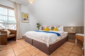 A bedroom with a bed, a chair, a radiator, a picture on the wall, and a window with curtains. - Semi-detached house lighthouse in vacation park with garden, terrace and pool - (Zingst)