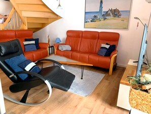 Una sala de estar moderna con un sofá, una silla, una mesita y un cuadro de un faro.