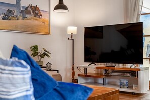 A living room with a flat-screen TV, a lamp, a painting, and a plant. - A premier townhouse in a vacation resort with a garden, terrace, and pool - (Zingst)