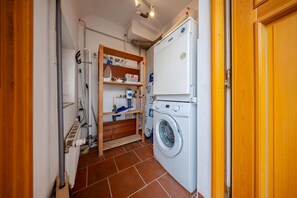 Une buanderie équipée d’un lave-linge, d’étagères contenant des produits de nettoyage et d’un étendoir en bois.