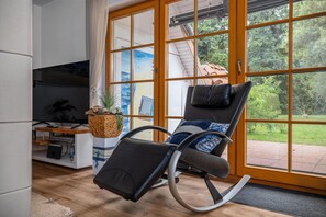 Een moderne woonkamer met een relax fauteuil, een flatscreen televisie en een grote schuifdeur naar een tuin.
