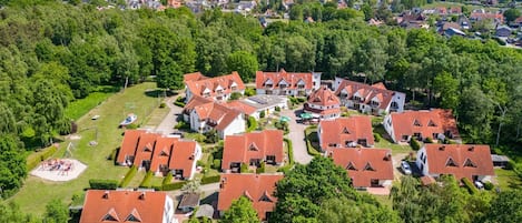 Un quartier résidentiel comprenant plusieurs maisons, une aire de jeux et un grand bâtiment doté d’un toit rouge.