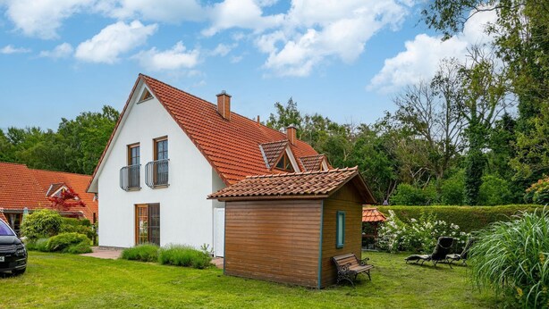 A two-story house with a red-tiled roof, a small wooden structure, and a well-maintained lawn.