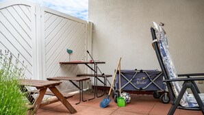 A patio with a wooden table, a folding table, a wheelbarrow, and a blue storage unit with a logo.