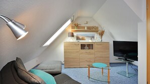Un dormitorio estilo loft acogedor con techo inclinado, un sofá, una mesa de centro de vidrio, un televisor y un aparador de madera.