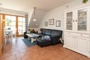 Una sala de estar con un sofá de cuero negro, un aparador blanco con puertas de vidrio y un comedor con mesa y sillas.