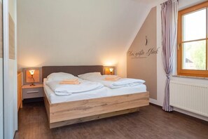 Ein Schlafzimmer mit einem hölzernen Bett, zwei Nachttischen mit Lampen, einem Fenster mit Vorhängen und einem Wandzeichen.