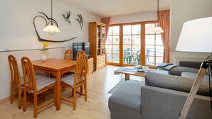 Ein modernes Wohnzimmer mit Esstisch aus Holz, grauem Sofa und Fernseher.