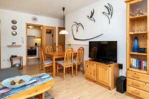 Una sala de estar acogedora con una mesa de comedor de madera, sillas, un televisor y una estantería.