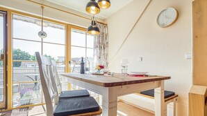 A dining area with a wooden table and chairs, a clock on the wall, and a view through large windows. - Comfortable Windrose vacation apartment with balcony, pool and garden view in Zingst - (Zingst)