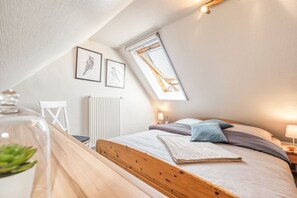 Ein gemütliches Schlafzimmer mit schrägen Wänden, einem Bett mit Kissen, einem Heizkörper und gerahmten Kunstwerken an der Wand.